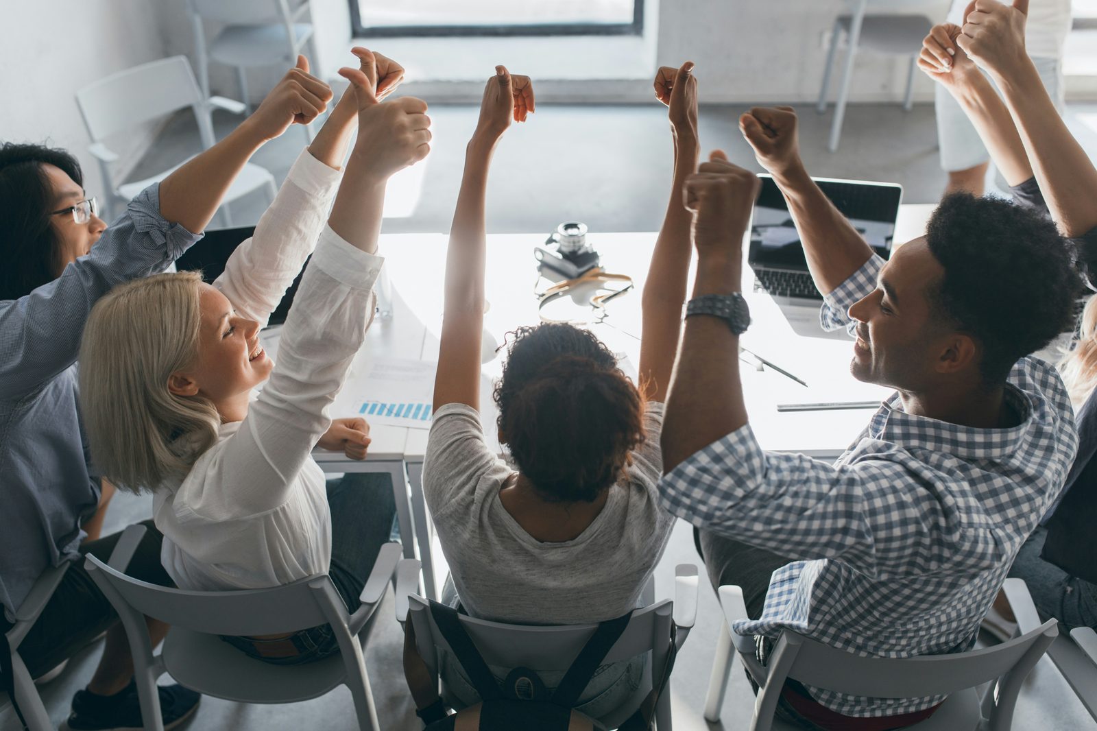 Diverse team of professionals celebrating a successful project outcome around a conference table